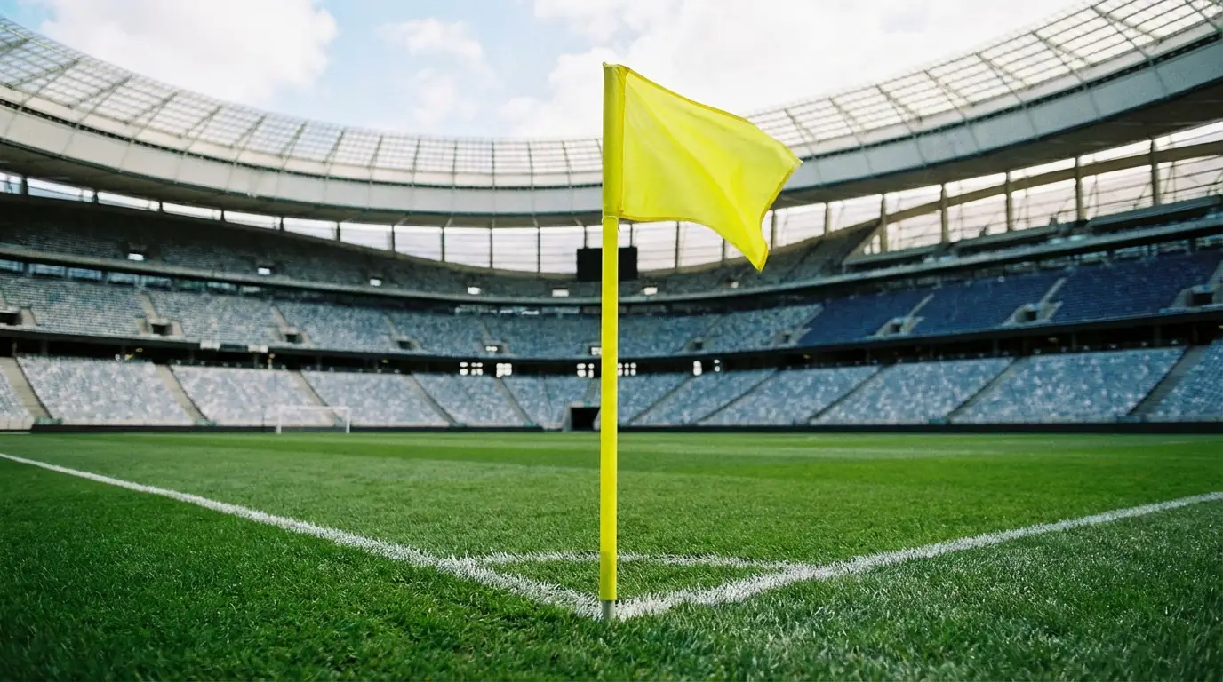 Eckfahne und Spielfeldecke eines Fußballstadions mit gepflegtem Rasen und leeren Rängen im Hintergrund